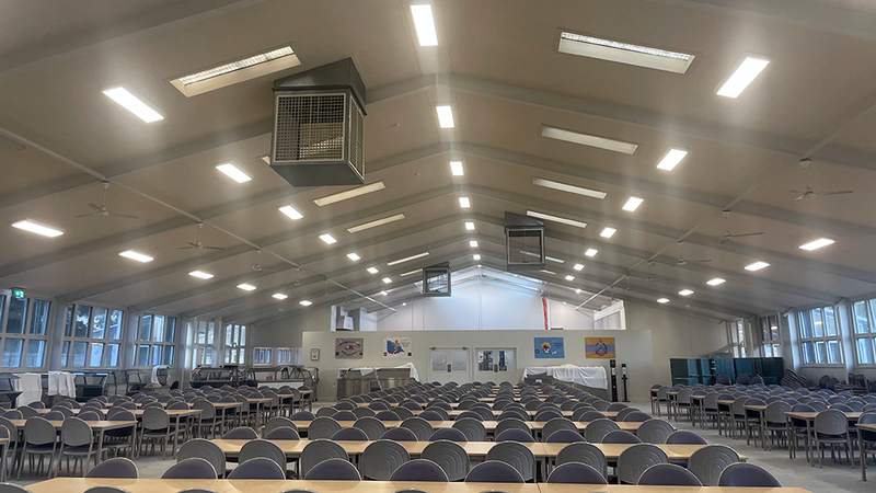 A large room with rows of tables and chairs illuminated by ceiling lights