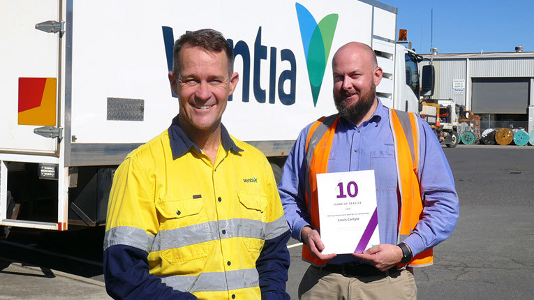 Two employees holding with certificate in high-visibility attire