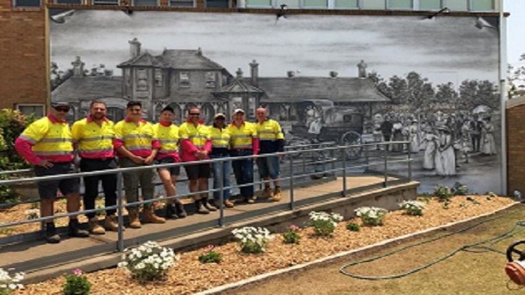 Visionstream team in uniform pictured in Kurri Kurri, Australia in front of a mural