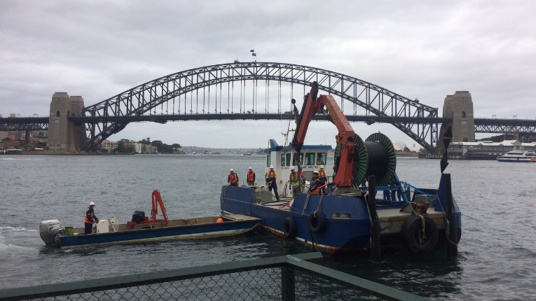 Sydney Harbour Bridge and harbour water with cloudy sky and Visionstream project equipment and workers